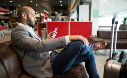 Business Mann mit Koffer sitzt auf Couch und schaut auf Smartphone
