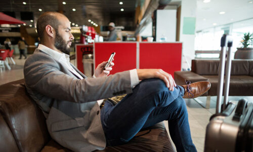 Business Mann mit Koffer sitzt auf Couch und schaut auf Smartphone