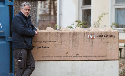 Mann vor Plakat von DMU Consult Ingenieurgesellschaft mbH - ehemalige Bayernkaserne Projektbüro