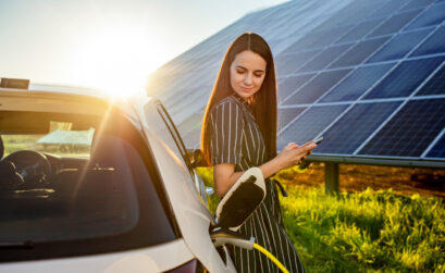 Frau lehnt lächelnd an tankendem Auto, Solarzellen im Hintergrund