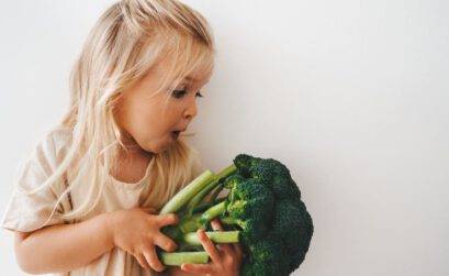 Kleines Mädchen bestaunt Brokkoli-Kopf mit einem beeindruckten Gesichtsausdruck