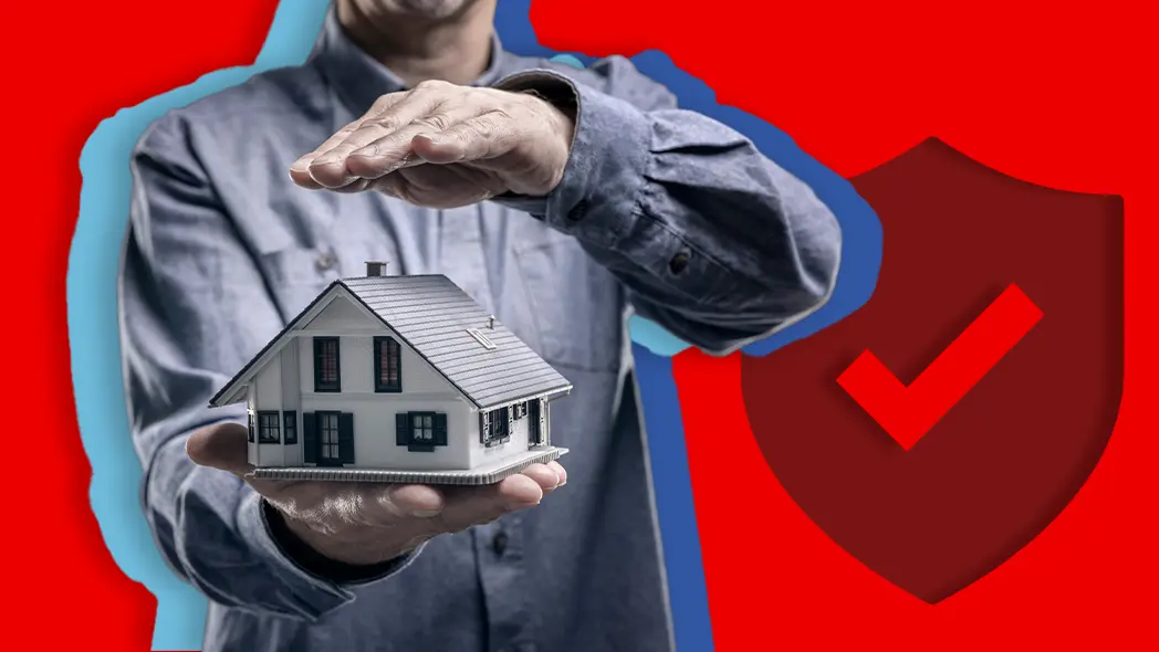 Versicherungen fürs Eigenheim: Mann hält schützend seine Hände über ein detailliertes Modellhaus, im Hintergrund ein rotes Schild mit einem Haken als Symbol für optimalen Versicherungsschutz.